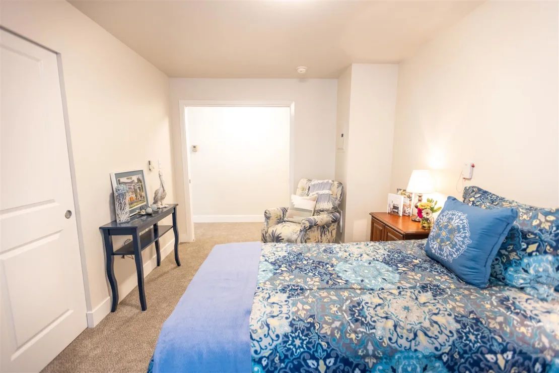 A cozy bedroom featuring a blue-patterned bedspread, a side table with a lamp, and decorative elements.