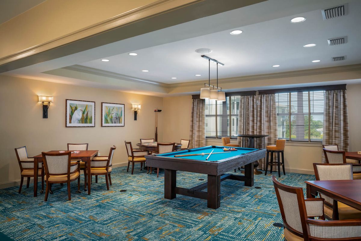 A well-lit game room featuring a pool table, surrounded by tables and chairs, with framed artwork adorning the walls.