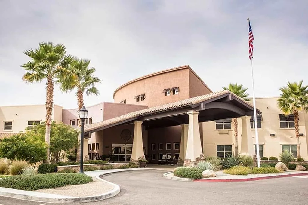 The image shows the entrance of a building with columns and palm trees, set against a clear sky.
