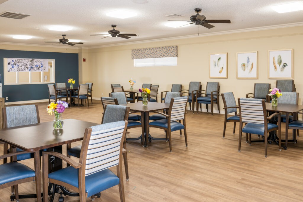 A bright and spacious dining room with neatly arranged tables and chairs, featuring decorative flowers on each table.