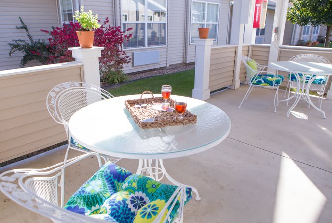 A cozy outdoor patio with a glass table, colorful cushions, and potted plants.
