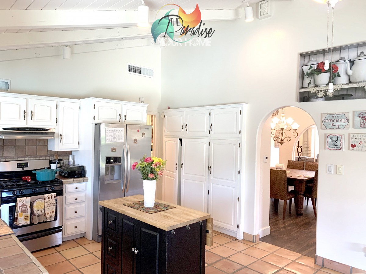 A bright, open kitchen with white cabinets and a central island, featuring stainless steel appliances and a view into the dining area.