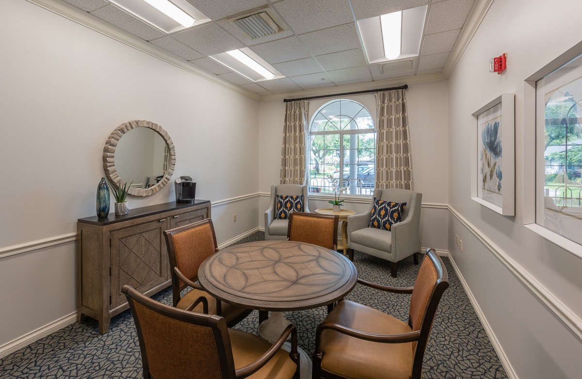 A cozy meeting room with a round table, surrounded by chairs, and a window bringing in natural light.