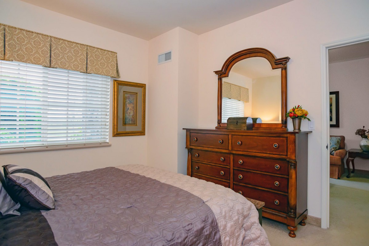 A cozy bedroom featuring a dresser with a mirror, a neatly made bed, and a window with curtains.