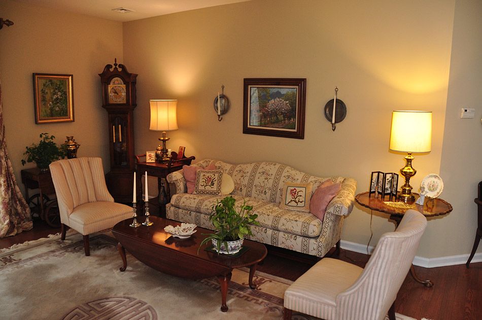 A cozy living room featuring traditional decor with a sofa, chairs, and a coffee table, accented by lamps and wall art.