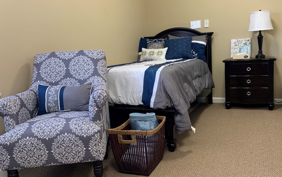 A cozy bedroom setup with a bed, patterned chair, and a basket filled with blankets.