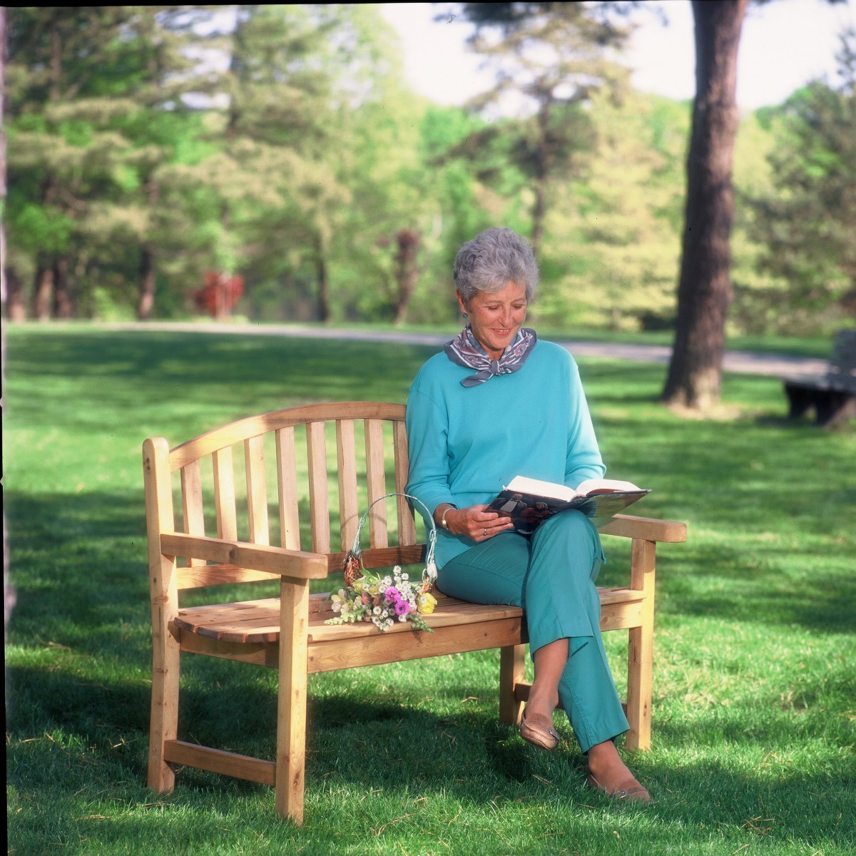 A woman sitting on a bench in a park, enjoying a book under the trees.