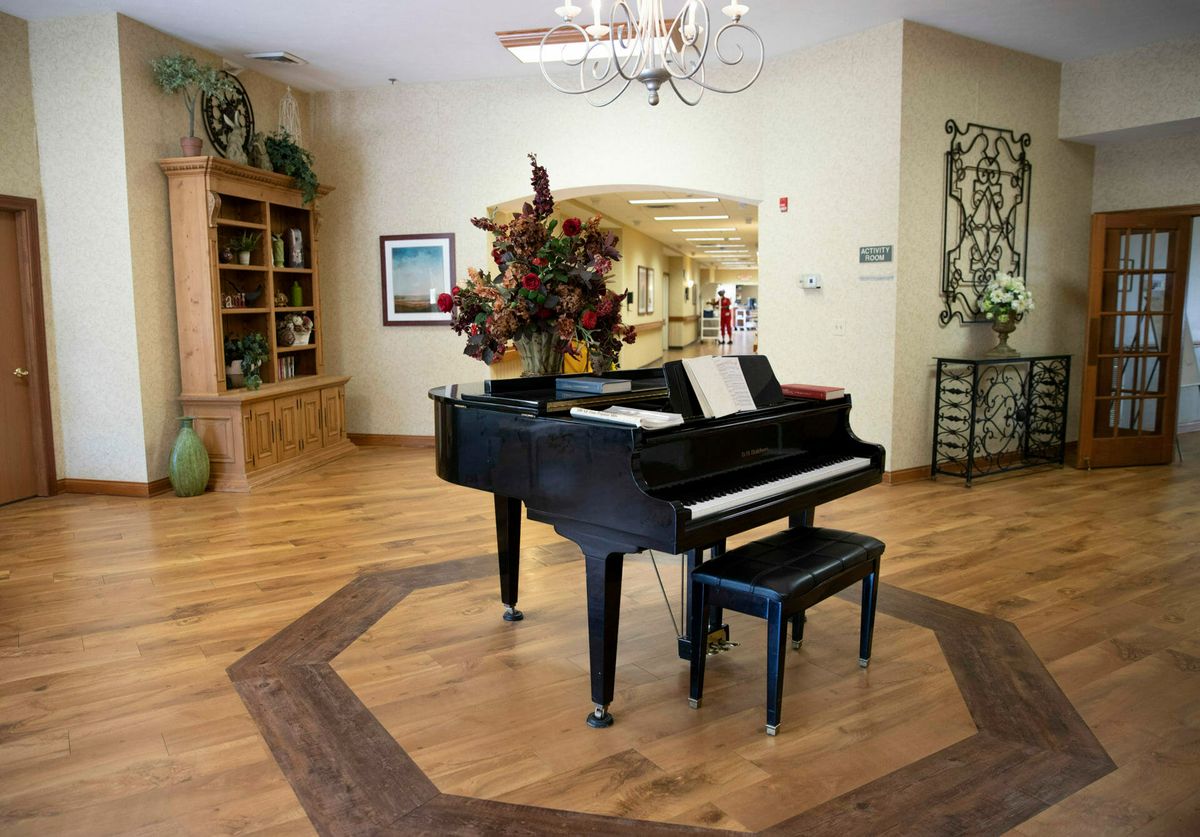 A grand piano is elegantly placed in a well-decorated living space featuring wood floors and a chandelier.
