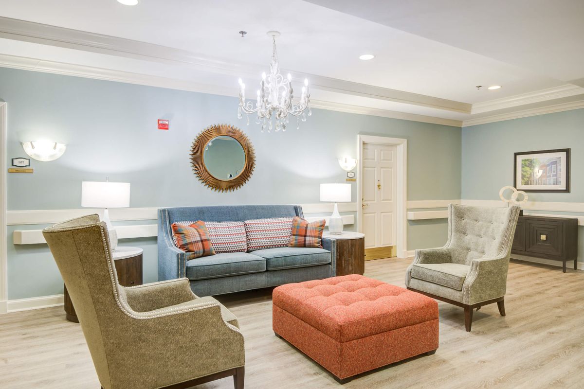 A cozy living room with a sofa, armchairs, and a large ottoman under a chandelier.