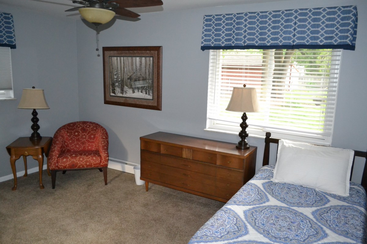 A cozy bedroom with a red chair, wooden chest, and bed beside a window.