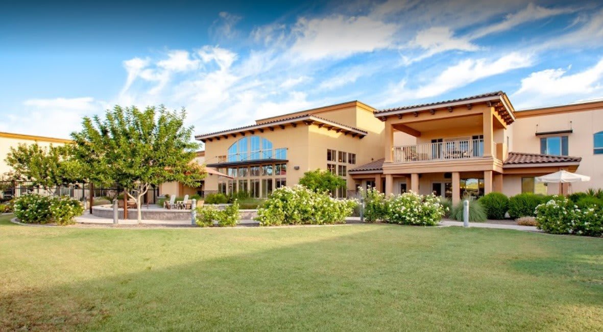 A large, modern building with a well-maintained lawn and landscaping under a partly cloudy sky.