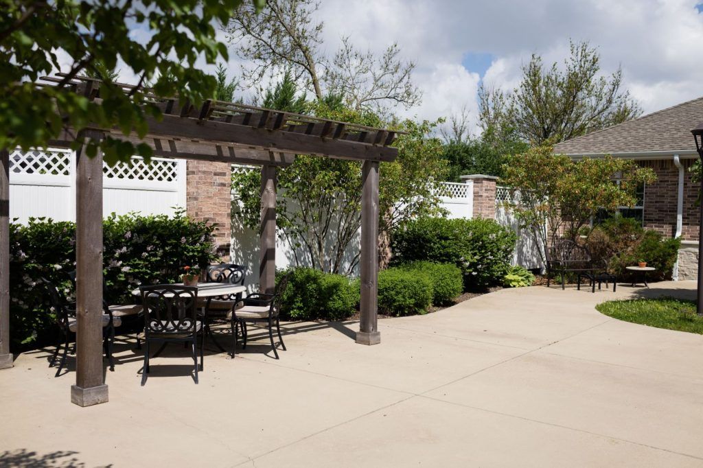 A sunny patio garden with a pergola and outdoor seating surrounded by lush greenery.