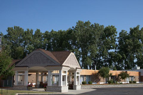 A building entrance with a canopy surrounded by trees under a clear blue sky.