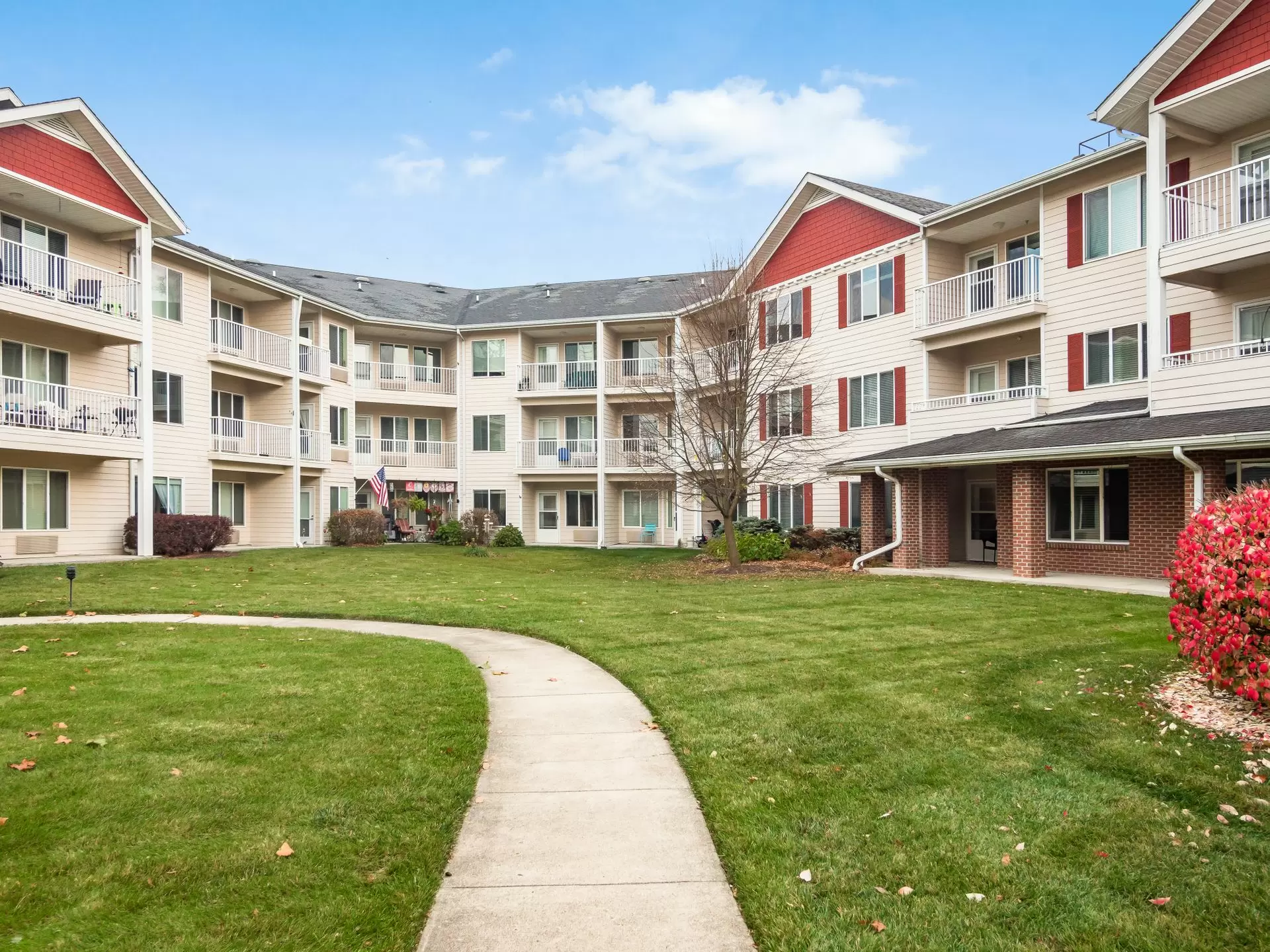 A three-story residential apartment building with a well-maintained lawn and pathway under a clear blue sky.