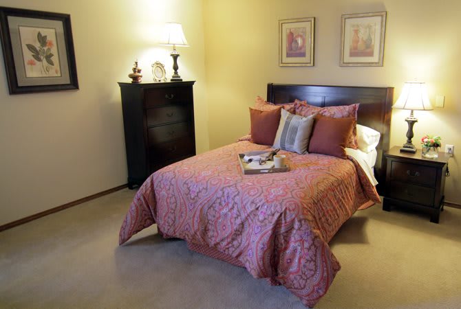A cozy bedroom with a neatly made bed, decorative pillows, a bedside lamp, and framed pictures on the wall.