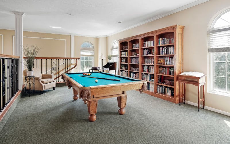 A bright room featuring a pool table and extensive bookshelves.