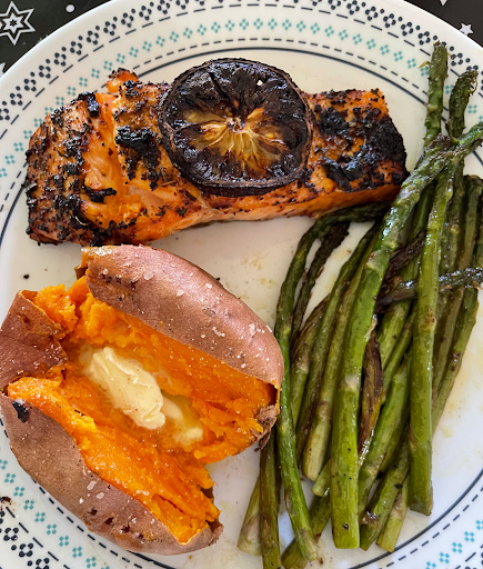 A delicious and healthy dinner plate featuring grilled salmon with lemon, a fluffy sweet potato, and fresh asparagus.