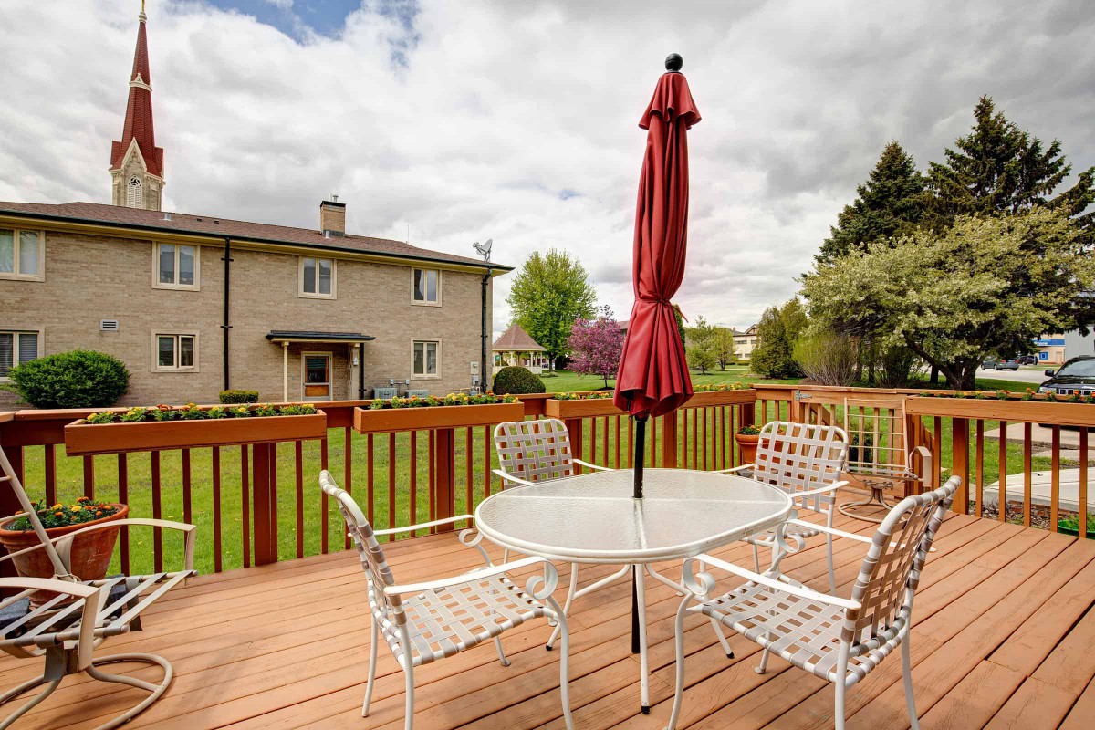 Outdoor patio with seating area and a red umbrella overlooking a spacious backyard.