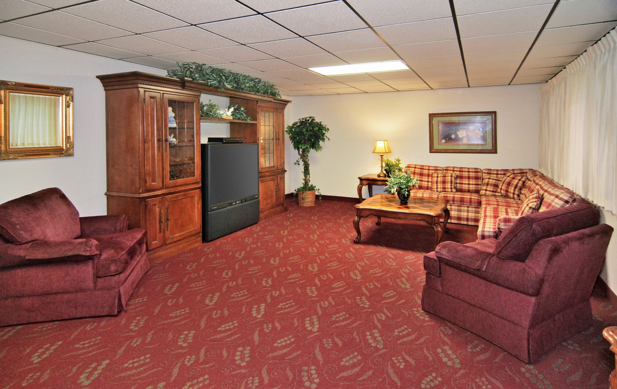 A cozy living room with a plaid sofa, wooden furniture, and red carpet.