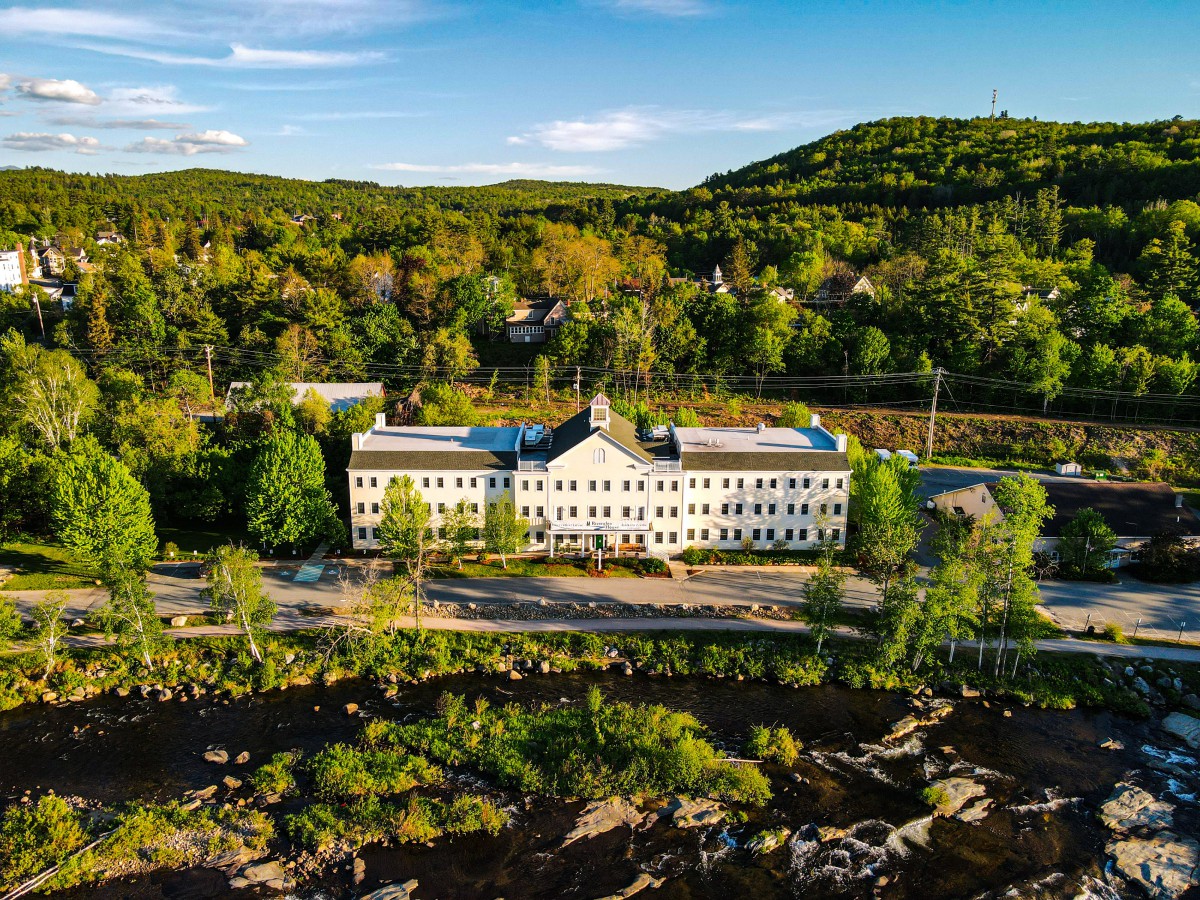 An aerial view of a large building surrounded by lush trees and rolling hills under a clear blue sky.