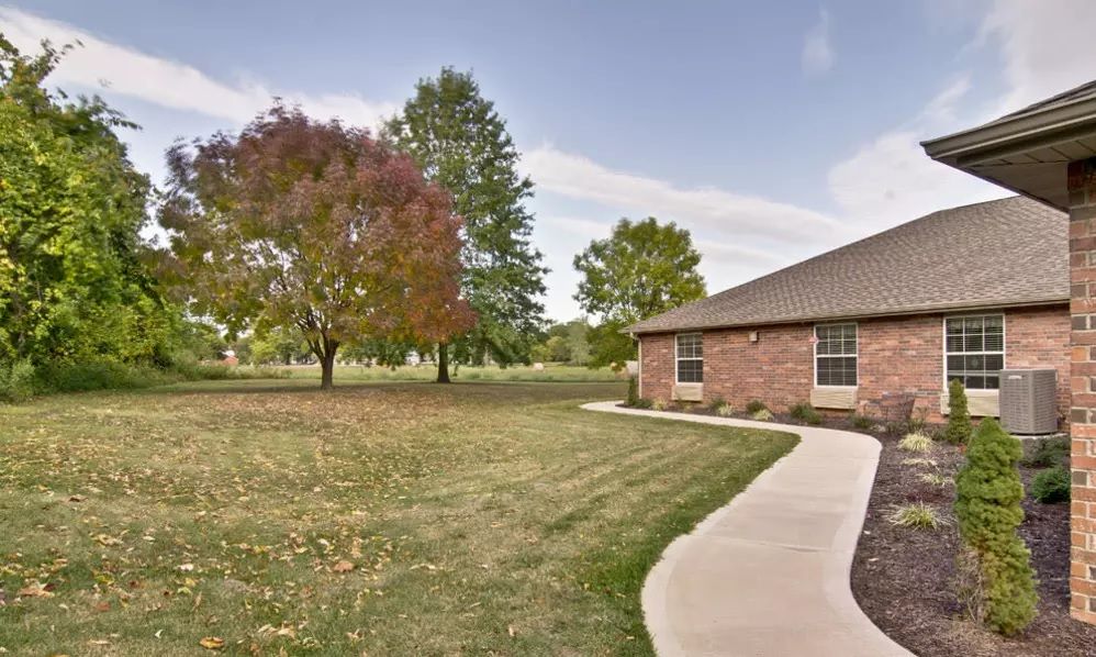 A brick house with a well-maintained lawn and trees, featuring a curved sidewalk leading to the entrance.