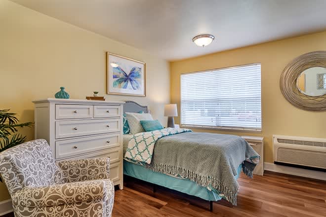 A cozy bedroom with a bed, dresser, and a large window providing natural light.