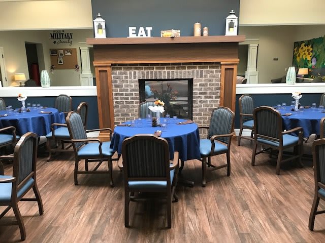 A cozy dining area with blue tablecloths, a central fireplace, and inviting decor.