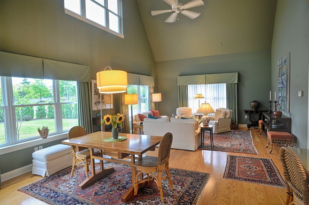 A spacious living room with a dining area, showcasing modern decor, wood flooring, and large windows offering ample natural light.