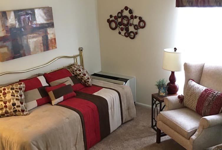 A cozy bedroom with modern decor, featuring a neatly made bed, wall art, and a lamp on a side table.
