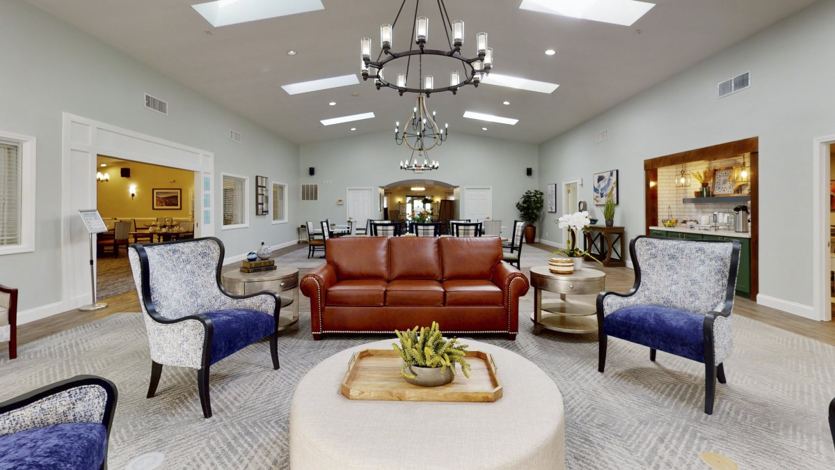 A spacious and elegantly decorated living room featuring a central leather sofa, two armchairs, chandeliers, and a coffee table with decorative items.