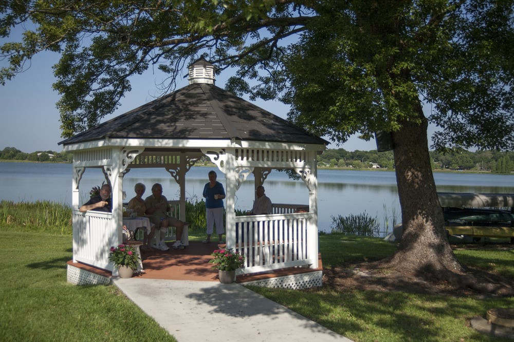 A group of people sitting in a gazebo by the lake, surrounded by trees and picturesque scenery.