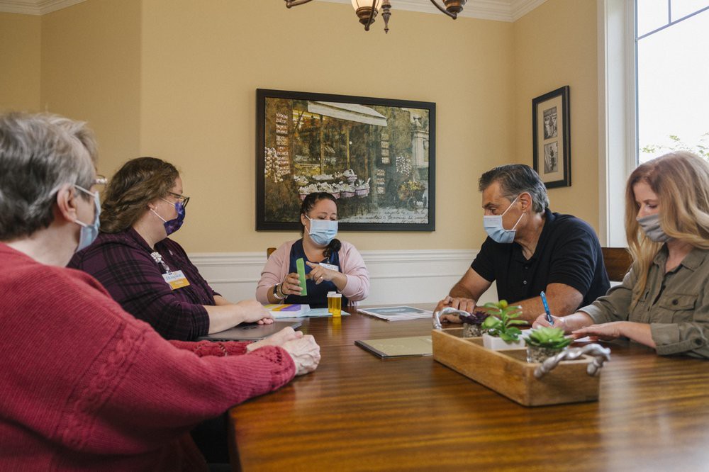 A group of people sit around a table having a discussion while wearing masks.
