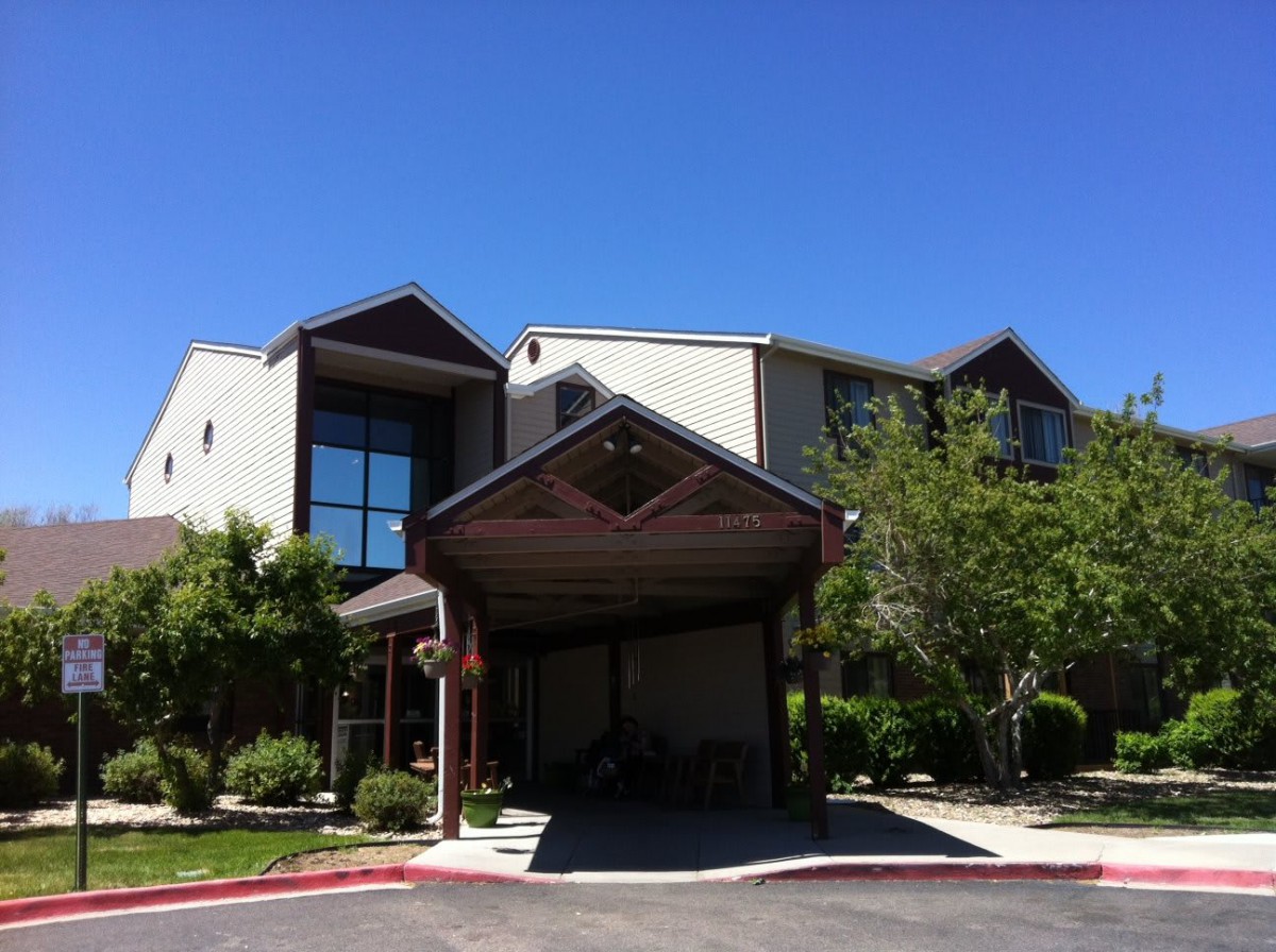 A sunny day view of a building entrance surrounded by greenery under a clear blue sky.