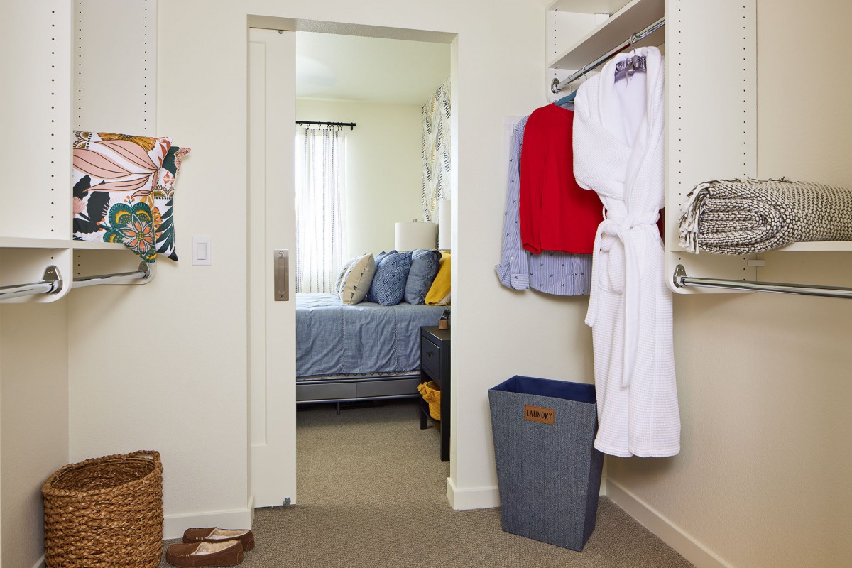 A neatly organized closet opens into a cozy bedroom with natural light.