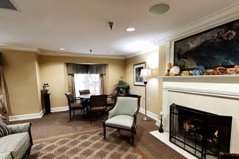 A cozy living room with a fireplace, chairs, and a table near a window.