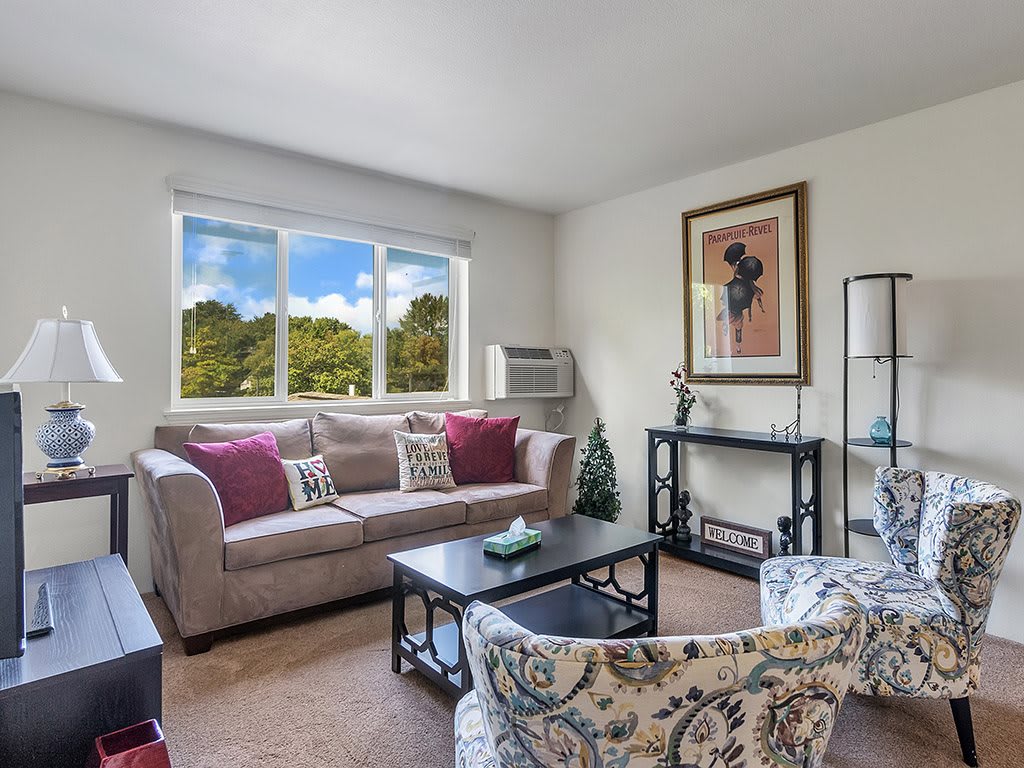 A cozy living room with a sofa, coffee table, and decorative artwork near a large window.