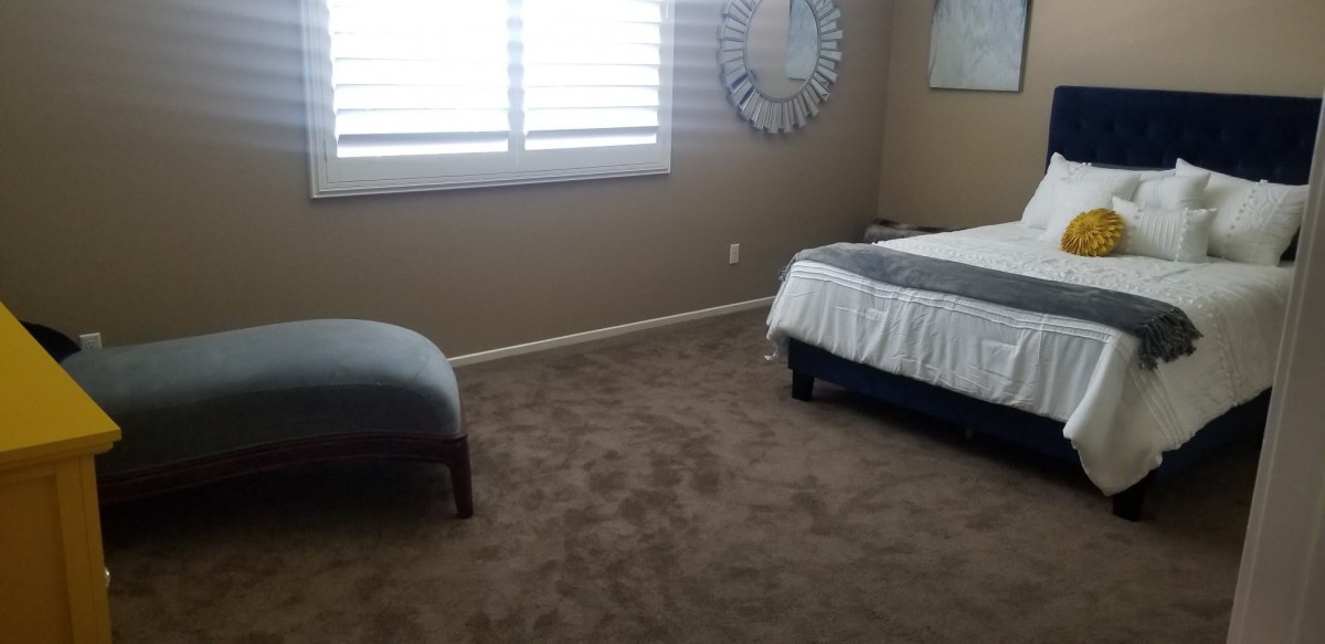 A neatly arranged bedroom with a bed, chair, and window with blinds.