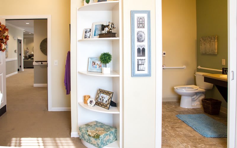 A home interior featuring a white corner shelf with decorative items, adjacent to a bathroom area.