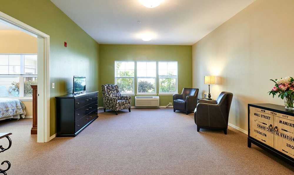 A modern living room with green walls, featuring a TV, chairs, and a large window.