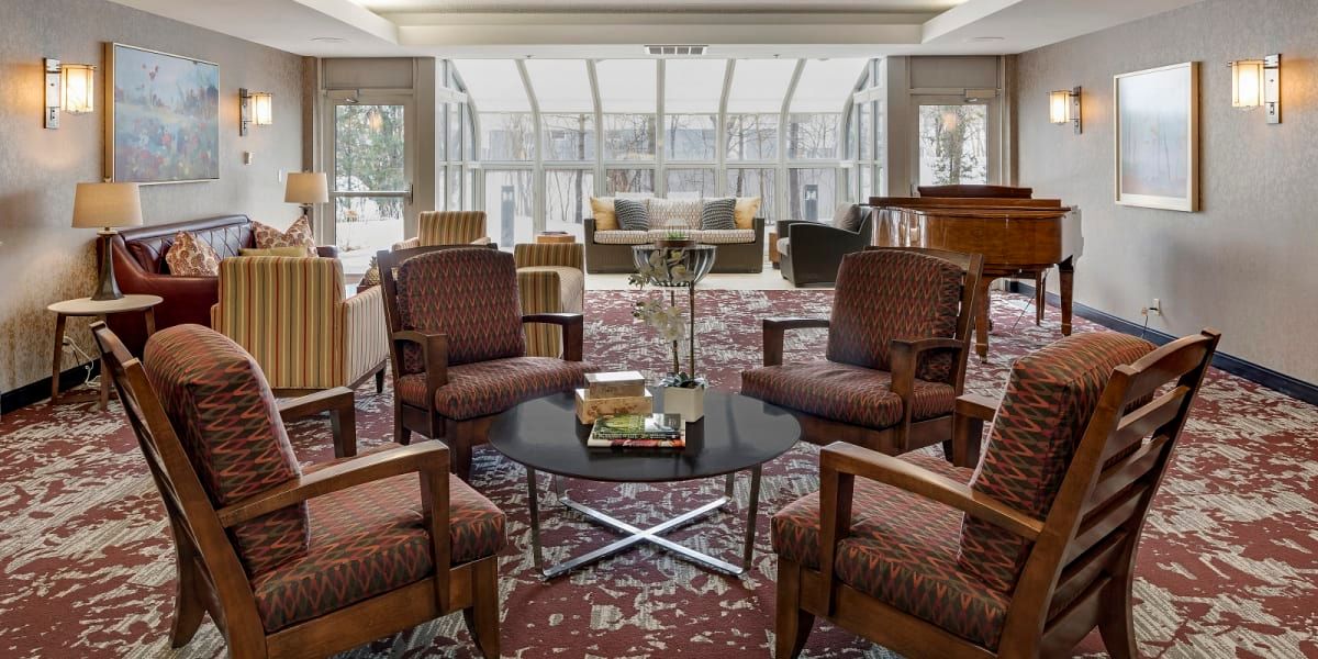 A spacious lobby with comfortable seating and a central table, featuring large windows in the background.