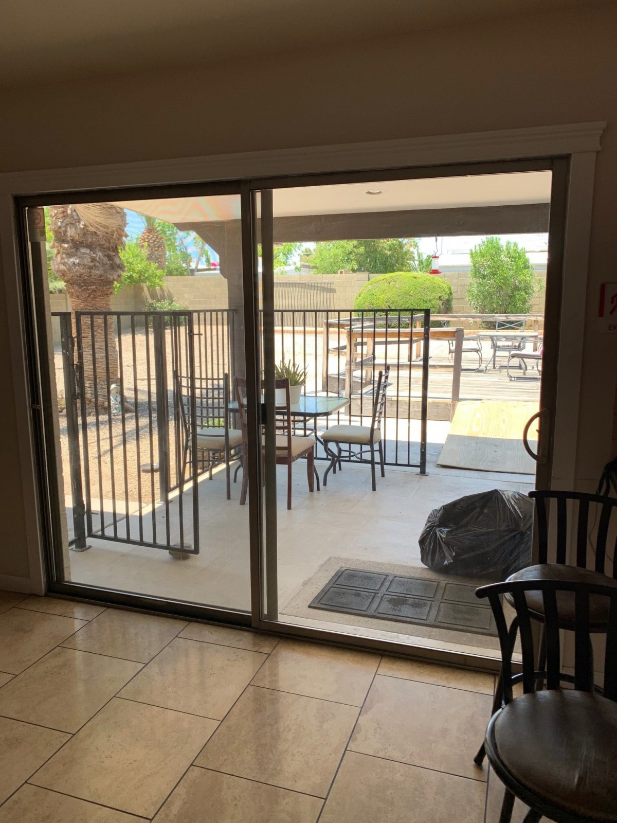 View from inside through a sliding glass door showing a patio with outdoor furniture and a metal fence.