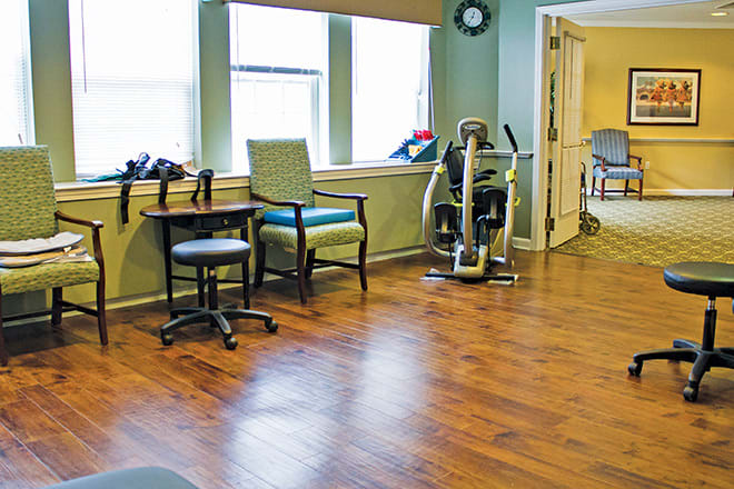 A brightly lit room with exercise equipment and chairs, featuring a hardwood floor.