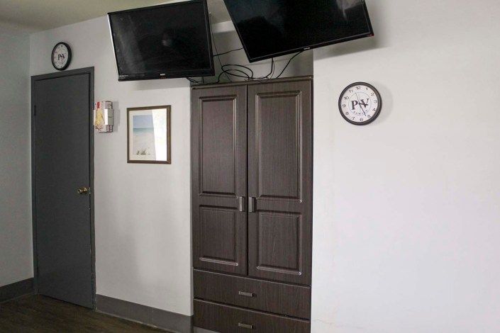 A hotel room with two mounted televisions, a wardrobe, and a clock on the wall.