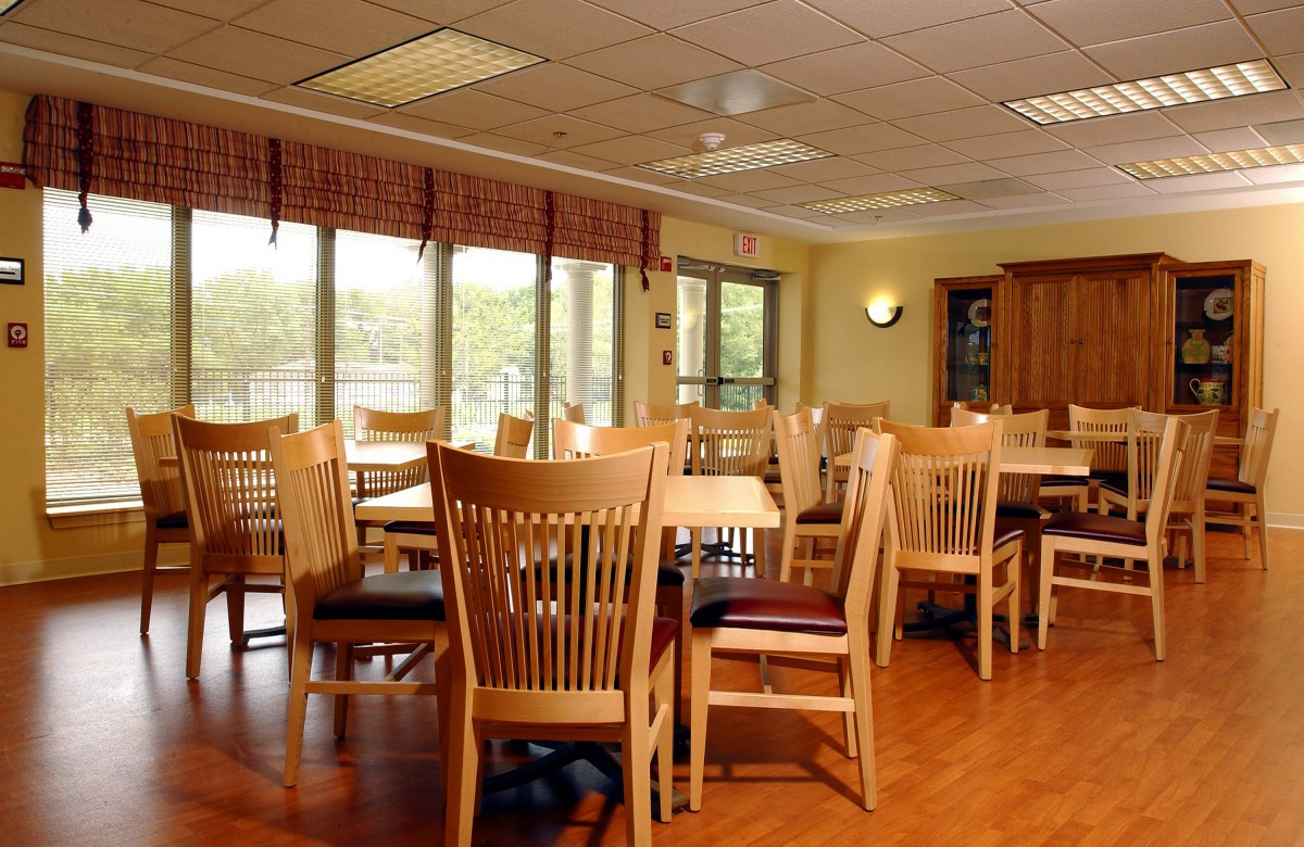 A bright dining room with wooden tables and chairs, featuring large windows that allow natural light to flood the space.