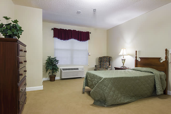 A neatly arranged hotel room with a single bed, a lamp on the bedside table, an upholstered chair, and a window with curtains.