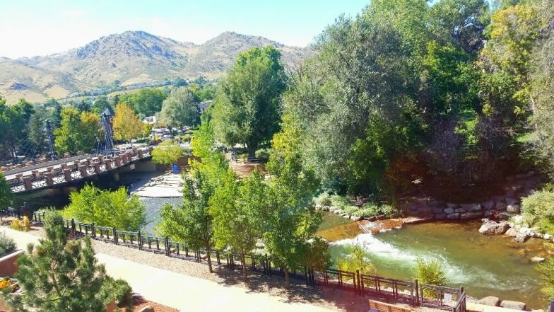 A scenic view of a river winding through a park with lush trees and mountains in the background.