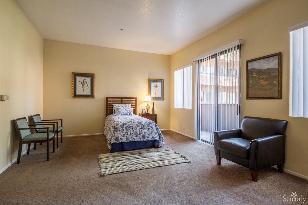 A cozy bedroom featuring a single bed, minimalist decor, and a flood of natural light from large windows.