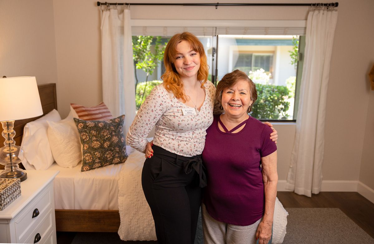 Two people smiling inside a bedroom.