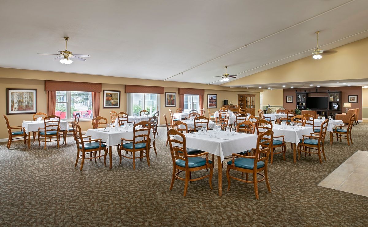 A spacious dining room with neatly arranged tables and chairs, featuring large windows and warm decor.