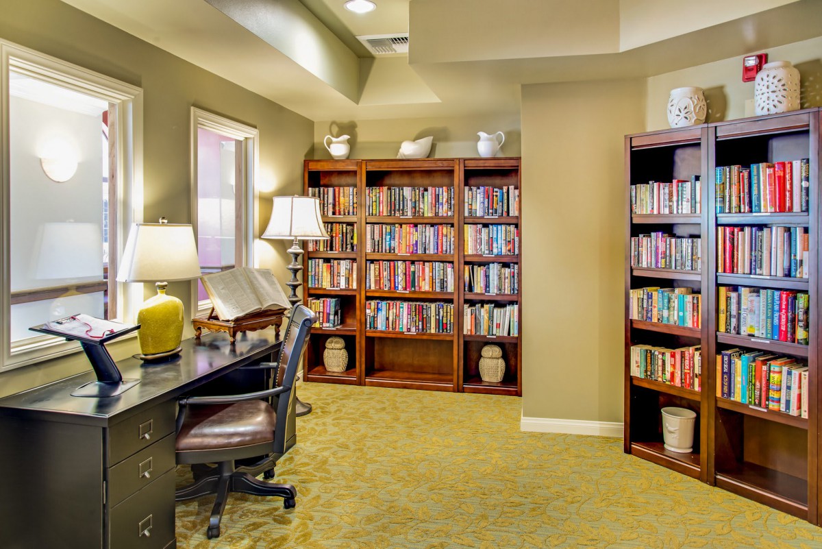 A cozy library corner with bookshelves, a desk, and a reading lamp.